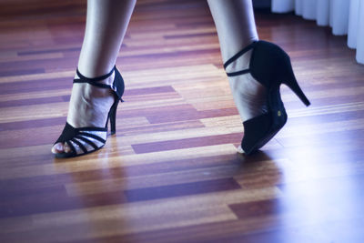 Low section of woman wearing high heels standing on hardwood floor