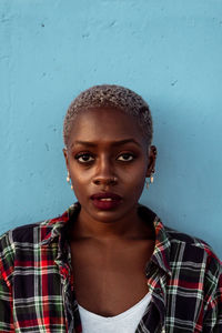 Young african american female with short hair and piercing wearing black plaid shirt looking at camera with intense eyes and challenge while feeling sad