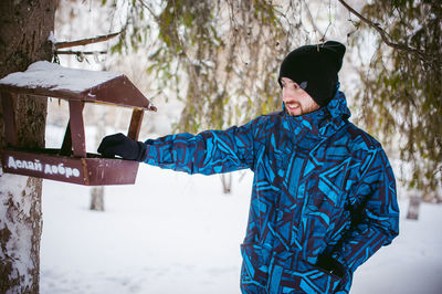 Young man standing by bird feeder on tree during winter