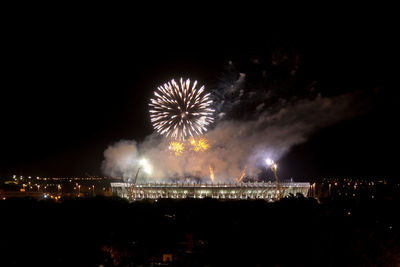 Firework display over city against sky at night