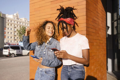 Smiling woman looking at friend using smart phone on street