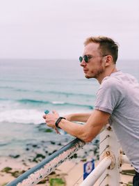 Side view of young man with bottle standing on pier at beach