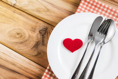 High angle view of red heart shape in plate by spoon and fork on table