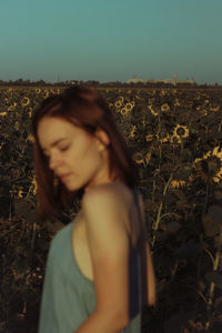 Young woman looking away while standing on field against sky