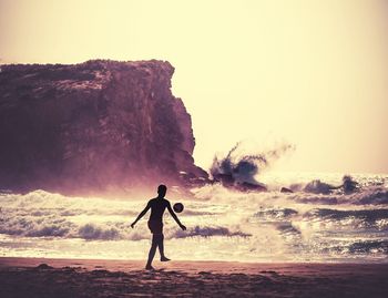 Silhouette man playing with ball at beach against clear sky