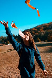 Girl throwing autumn leaves while standing on land