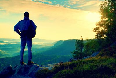 Silhouette of tourist. hiker with sporty backpack stand on rocky view point above misty valley.