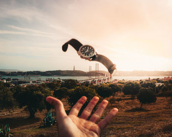 Midsection of person holding umbrella against sky during sunset