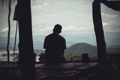 Rear view of silhouette man sitting on mountain against sky