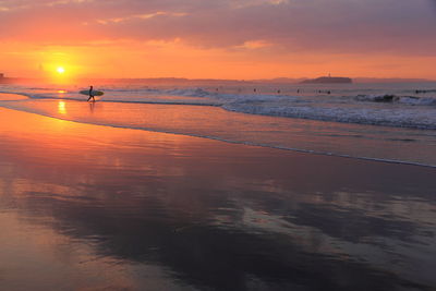 Scenic view of surfer on beach during sunset
