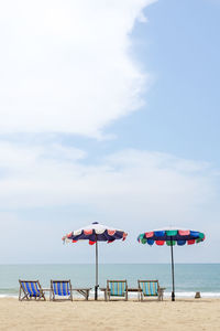 Deck chairs on beach against sky