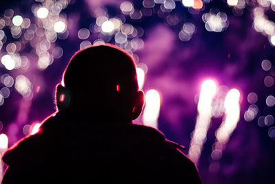 Rear view of silhouette person against illuminated lights and fireworks during festival at night