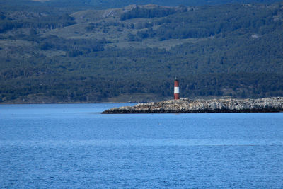 Lighthouse by sea and buildings against mountain