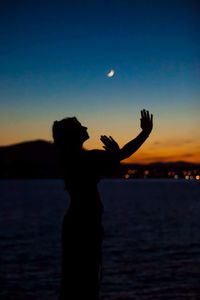 Silhouette hand against sea at sunset