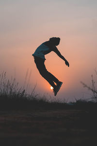 Silhouette man jumping on field against sky during sunset