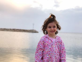 Smiling girl standing against sea during sunset