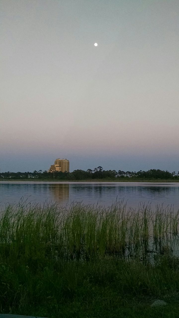 water, grass, lake, tranquility, tranquil scene, clear sky, sky, scenics, beauty in nature, reflection, nature, copy space, river, plant, built structure, growth, architecture, field, idyllic, building exterior