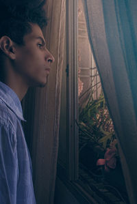 Side view of thoughtful man looking through window from house