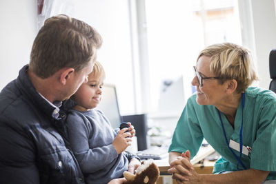 Smiling mature doctor talking to boy with father in clinic