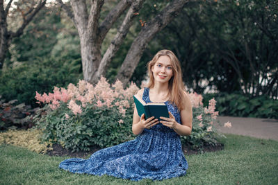 Smiling young woman reading book while sitting on field