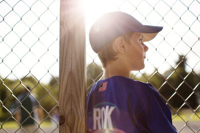 Baseball player looking away while standing by fence