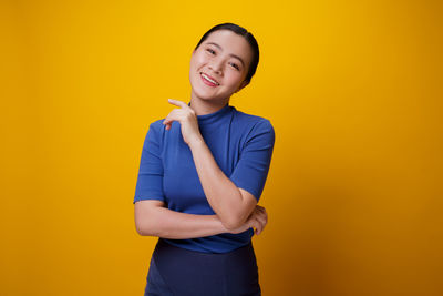 Smiling young woman standing against yellow background