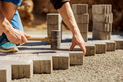 Young man laying gray concrete paving slabs in house courtyard on gravel foundation base. 