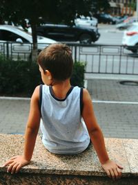 Rear view of boy sitting on retaining wall