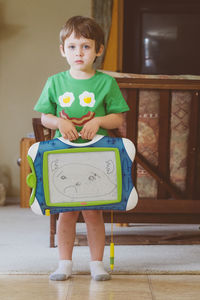 Portrait of cute boy holding slate standing at home