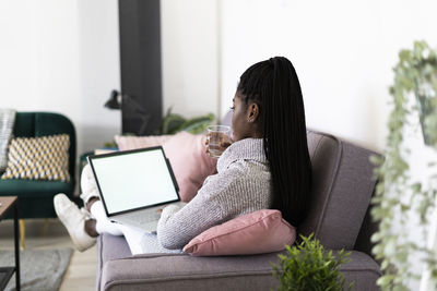 Young businesswoman drinking water working on laptop sitting at home