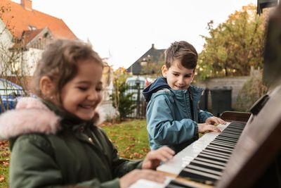 Smiling girl playing piano with brother in backyard