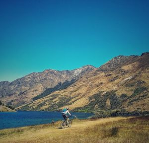 Man riding bicycle by lake against mountain