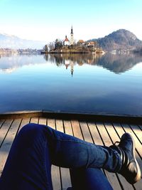 Low section of man sitting by lake against sky