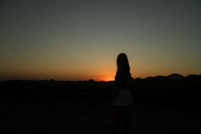 Rear view of silhouette woman standing on field against sky during sunset