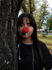 Woman with painted face looking away by tree trunk