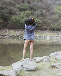 Rear view of woman standing on rock by lake