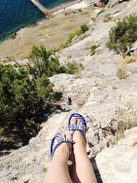 Low section of woman on cliff at beach during sunny day