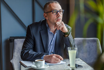 Thoughtful businessman writing on diary in cafe