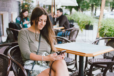 Young woman using mobile phone while sitting on table