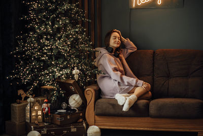 Young woman with headphones listens music from vinyl record, christmas tree in evening, eyes closed