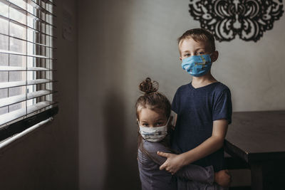Lifestyle portrait of young siblings with masks on hugging at home negative space