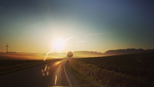 People on road amidst field against sky during sunset
