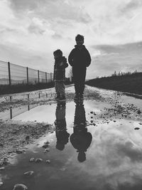 Rear view of men standing on puddle against sky