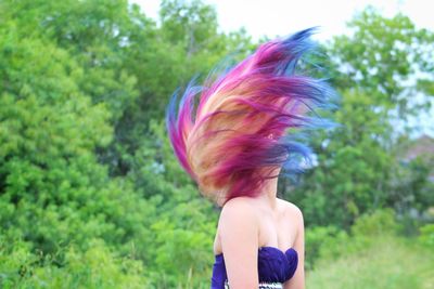 Woman tossing hair while sitting against trees in forest