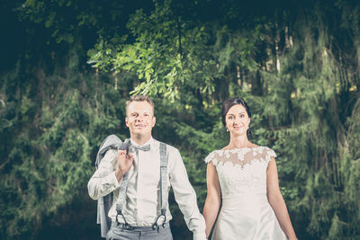 Portrait of smiling bride and groom standing against trees