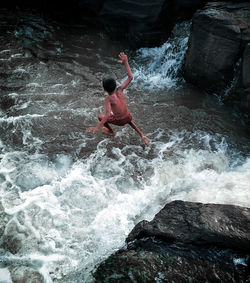 Rear view of man surfing on rock in sea