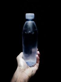 Close-up of hand holding glass bottle against black background