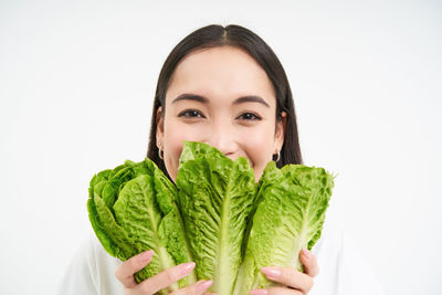 Portrait of smiling young woman holding leaf against white background