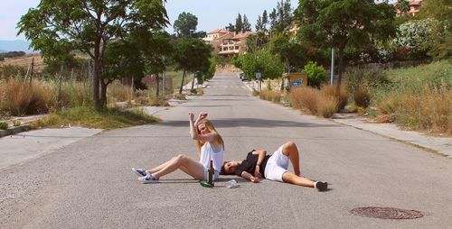 Full length of young woman sitting on road against trees