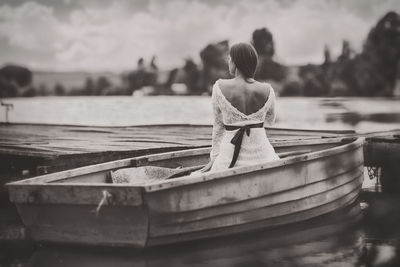 Rear view of bride sitting in boat by pier on lake